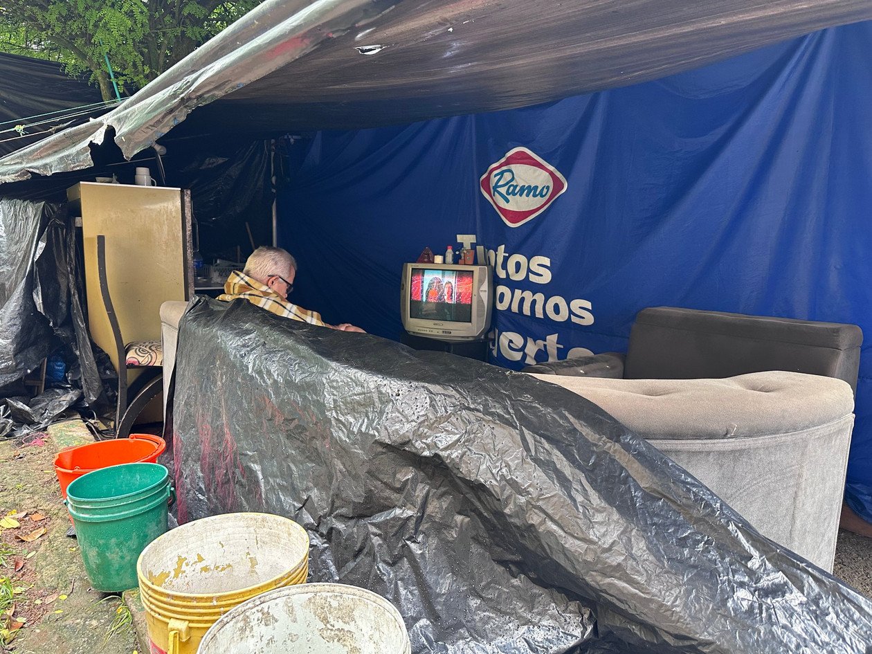 Hombre cubierto con una cobija mira televisión dentro de una carpa en Altos de Santa Elena, Cali