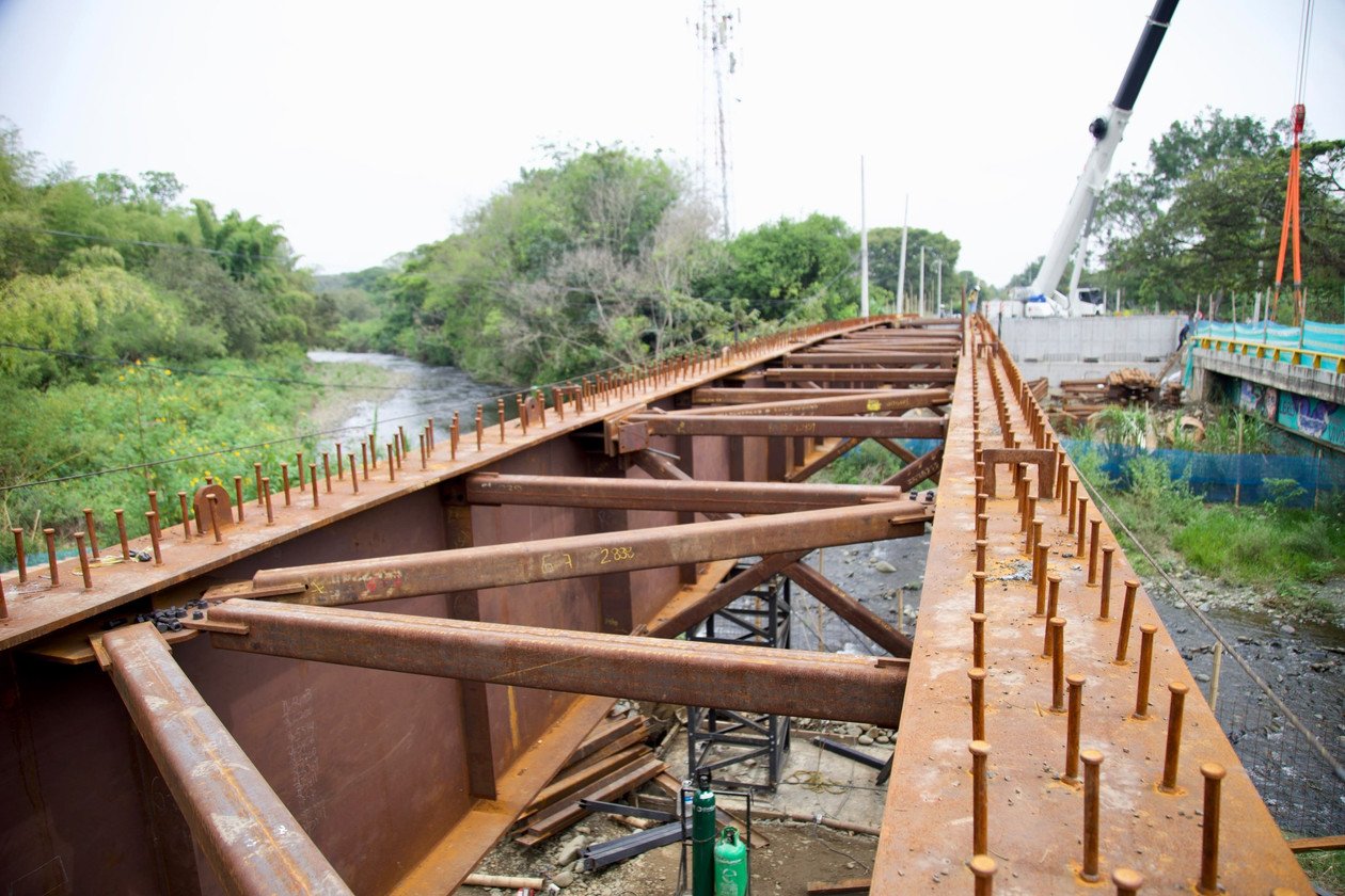 Estructura metálica del puente sobre el río Pance con sus vigas y arriostramientos, la grúa y el río al fondo